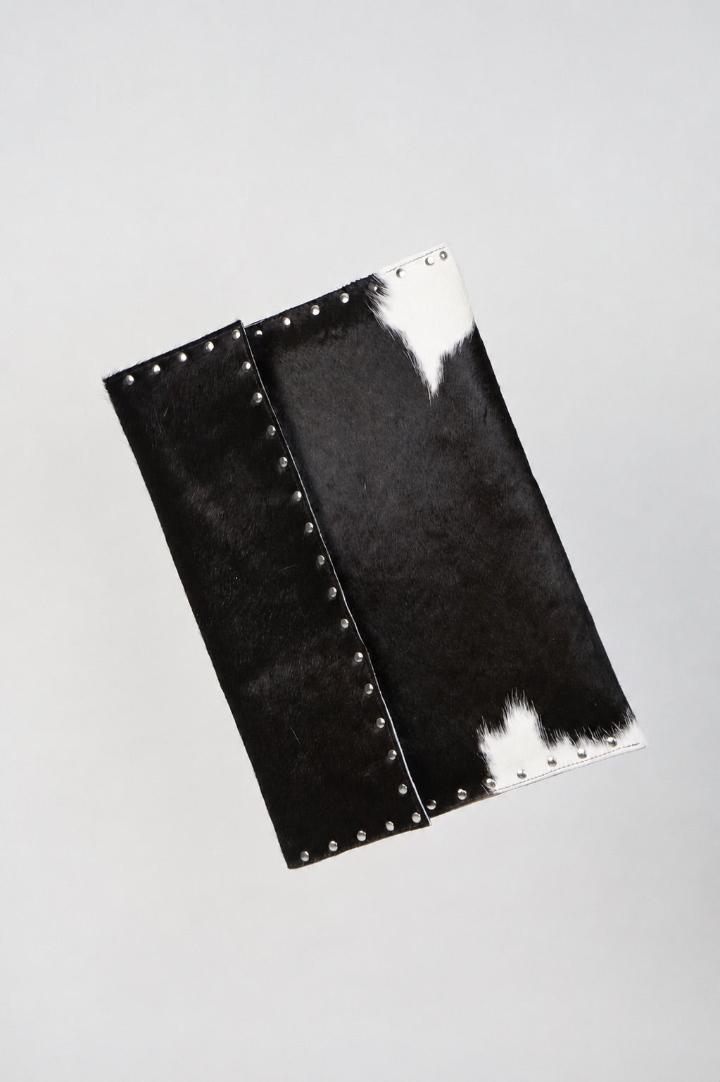 Black and white Cowhide laptop case by Violeta with silver stud trim, front view showing the flap