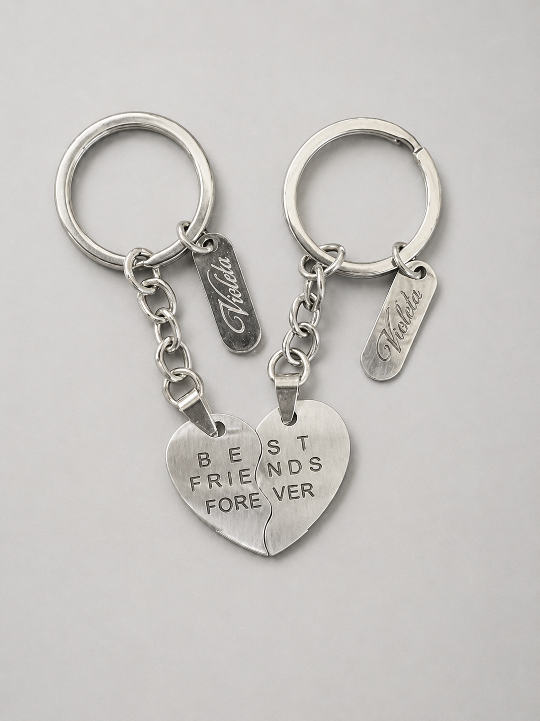 Two silver split-heart keychains with engraved text reading 'BEST FRIENDS FOREVER' and personalized name tags, displayed on a light gray background.