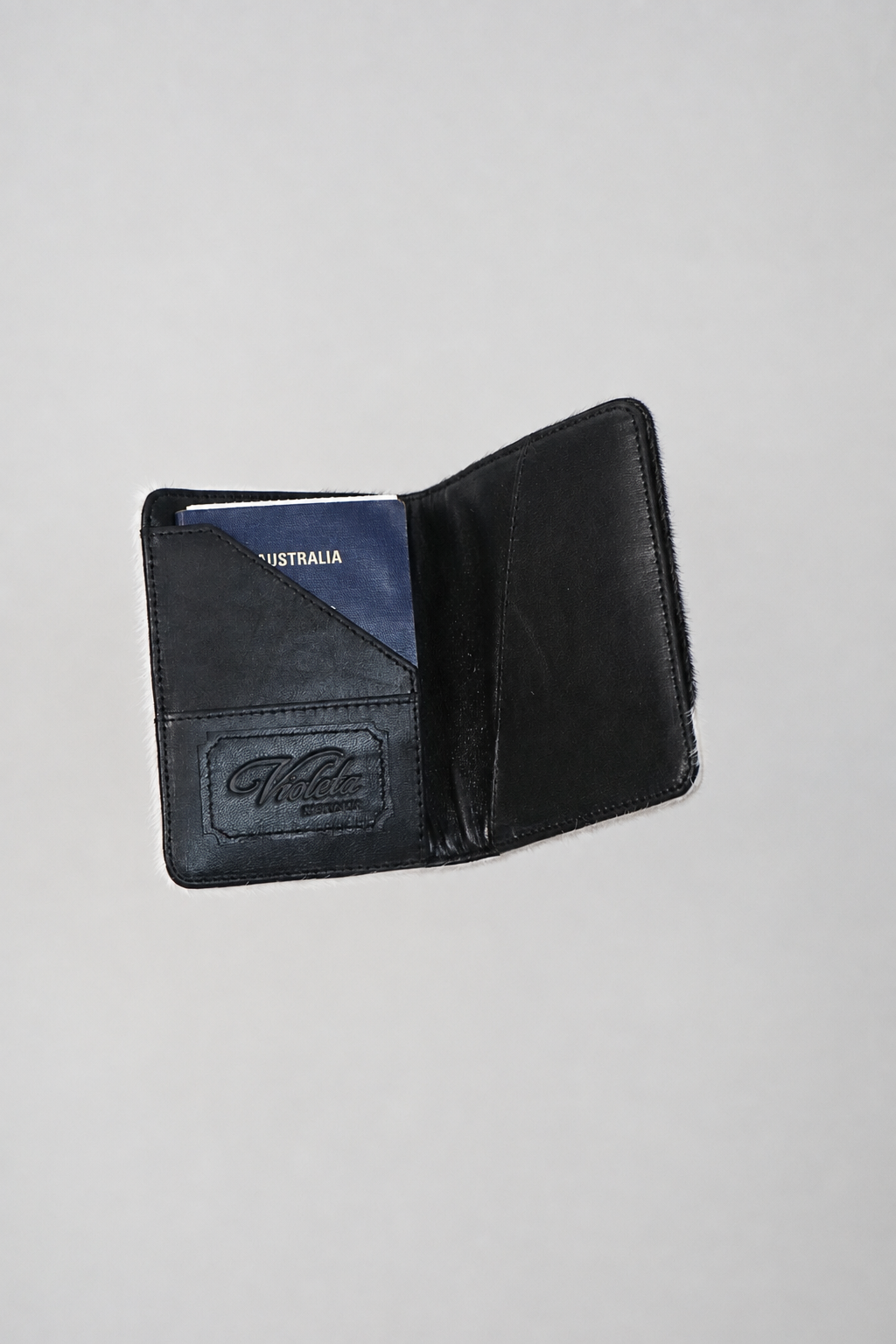 Cowhide passport case open with a passport inside and the embossed Violeta logo on the card slot