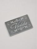 A rectangular mirrom card with rounded corners, featuring the word 'Violeta' in white cursive script and white decorative flourishes, photographed on a light gray background.