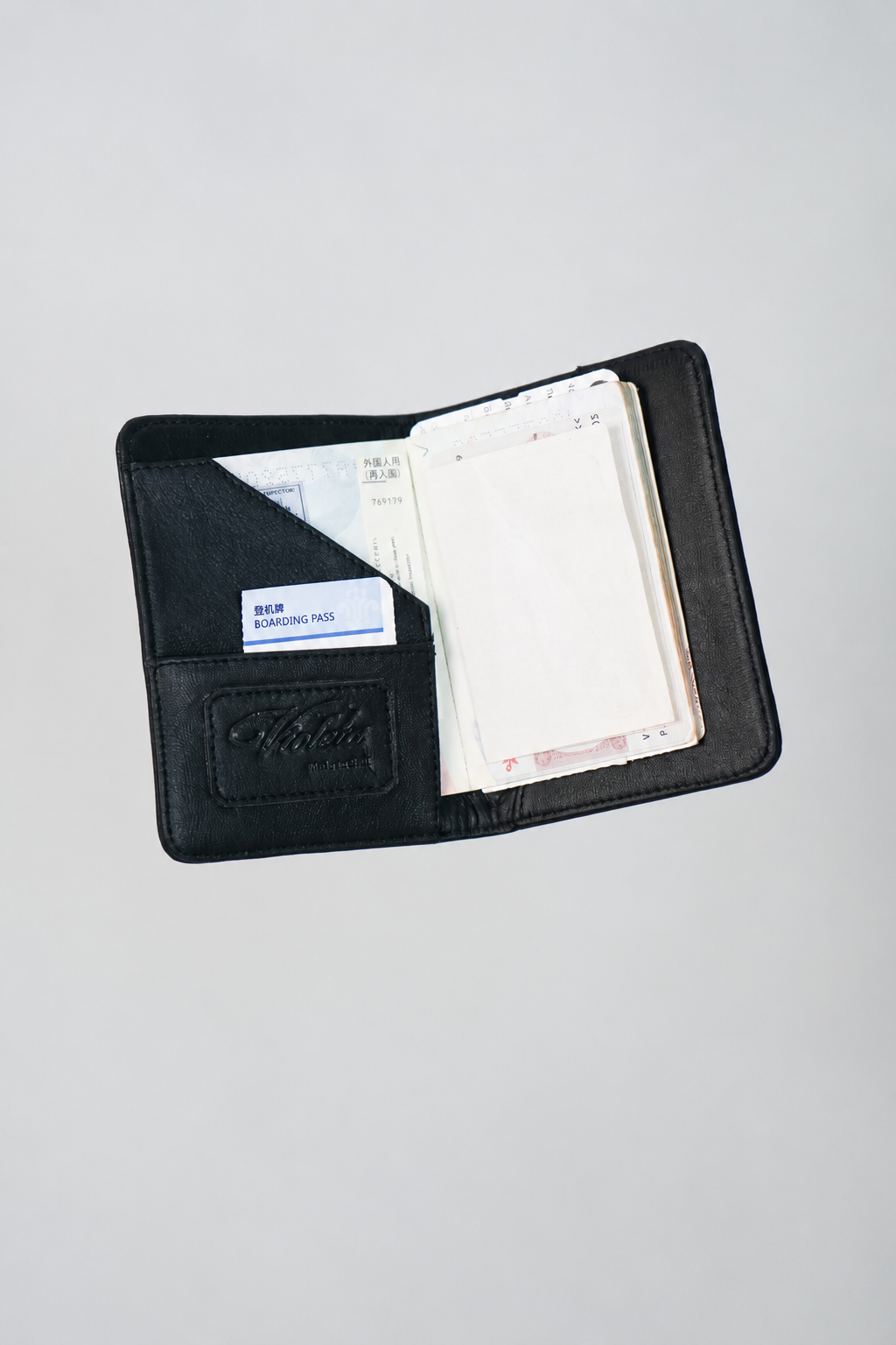 Shalom passport case open with a passport inside, a boarding pass in the front pocket and the embossed Violeta logo